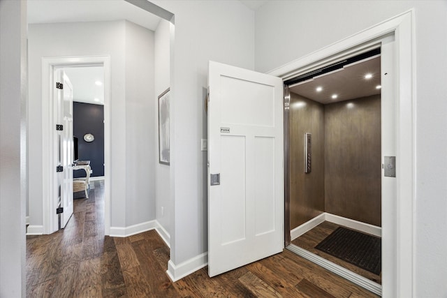 corridor featuring dark wood finished floors, elevator, and baseboards