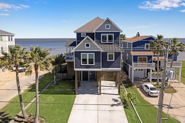 coastal inspired home featuring a water view, a balcony, a front lawn, and a shingled roof