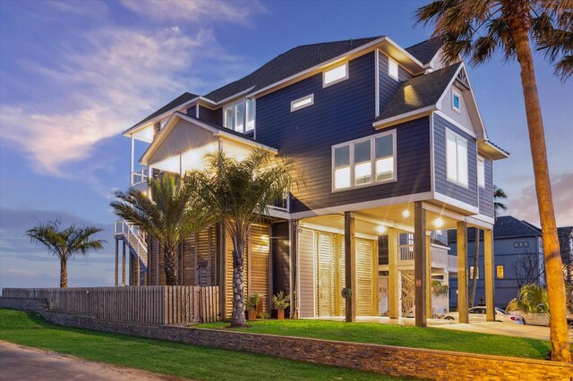 modern home with a yard, a shingled roof, and fence