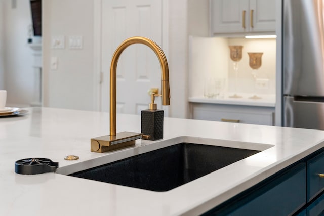 interior details with blue cabinetry, light countertops, a sink, and freestanding refrigerator