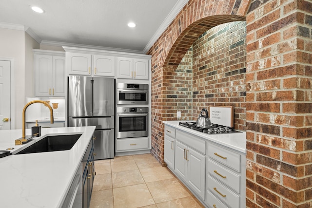 kitchen with brick wall, appliances with stainless steel finishes, a sink, and ornamental molding