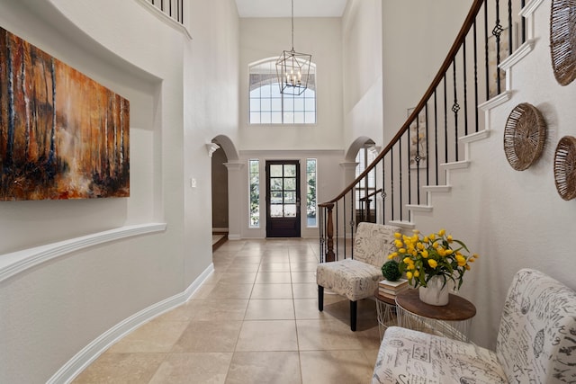 tiled entrance foyer with baseboards, arched walkways, an inviting chandelier, a high ceiling, and stairs