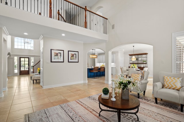 living room featuring arched walkways, a towering ceiling, baseboards, and light tile patterned floors