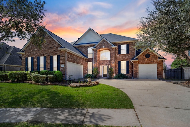 traditional-style house with a garage, brick siding, fence, concrete driveway, and a yard