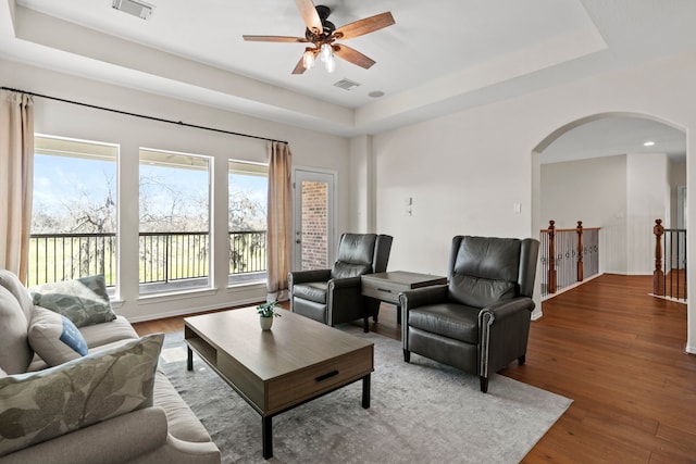 living area featuring arched walkways, a tray ceiling, wood finished floors, and visible vents