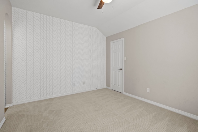 spare room featuring a ceiling fan, light carpet, vaulted ceiling, and baseboards