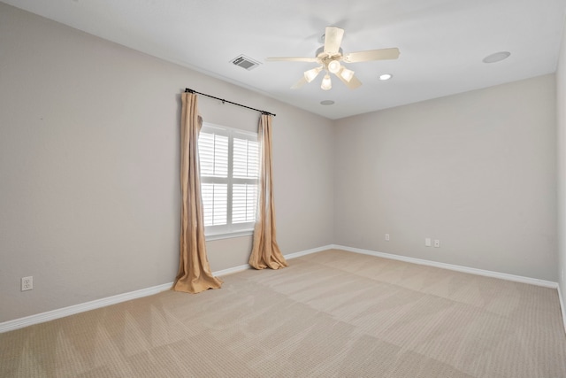 empty room with a ceiling fan, light colored carpet, visible vents, and baseboards