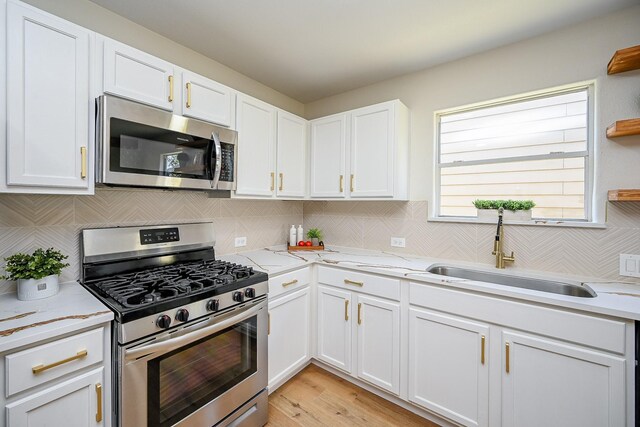 kitchen featuring a sink, stainless steel appliances, white cabinetry, tasteful backsplash, and light wood-type flooring