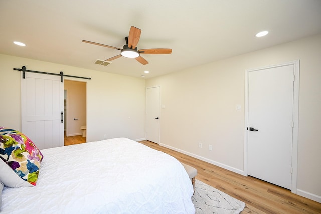 bedroom with a barn door, recessed lighting, visible vents, and light wood-type flooring