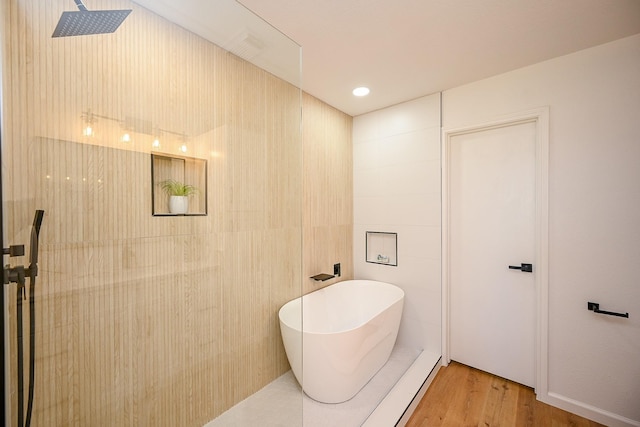 bathroom featuring wood finished floors, recessed lighting, a freestanding bath, walk in shower, and tile walls