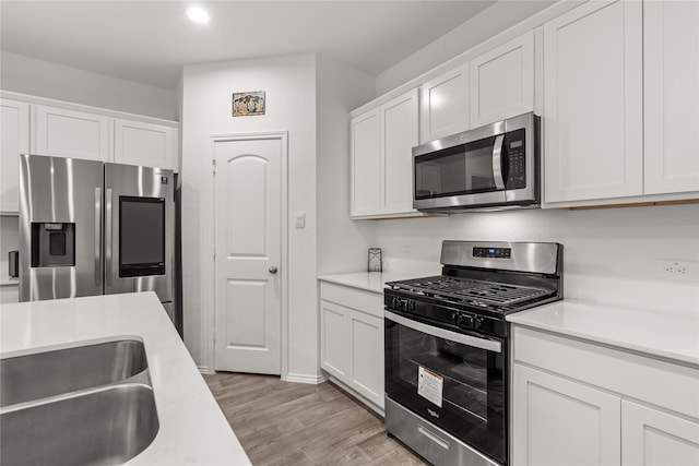 kitchen with appliances with stainless steel finishes, white cabinets, light countertops, and light wood-style flooring