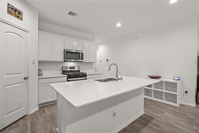 kitchen with white cabinets, appliances with stainless steel finishes, wood finished floors, a kitchen island with sink, and a sink