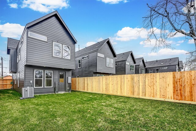 rear view of house featuring a lawn, central AC unit, and fence