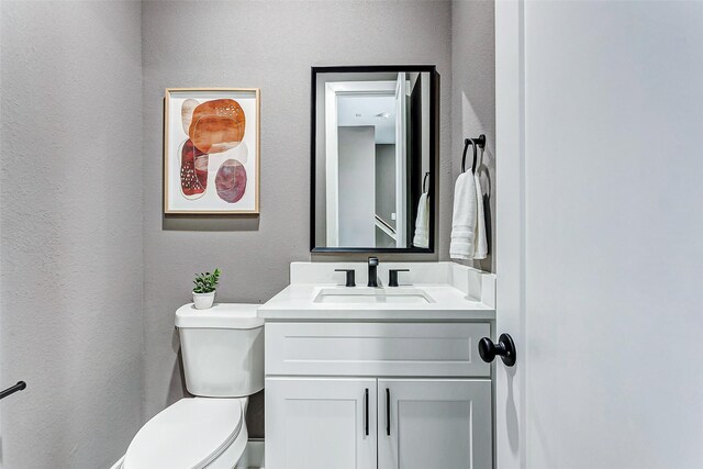 half bathroom featuring a textured wall, vanity, and toilet