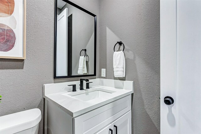 half bathroom featuring toilet, a textured wall, and vanity