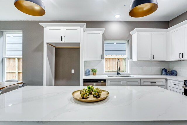 kitchen with light stone counters, decorative backsplash, white cabinets, a sink, and dishwasher