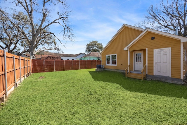 back of property with entry steps, a fenced backyard, cooling unit, and a lawn