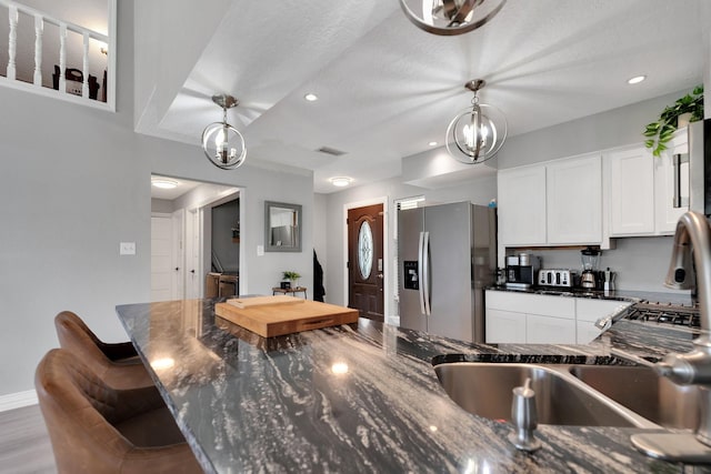 kitchen featuring stainless steel fridge, a chandelier, white cabinets, and decorative light fixtures