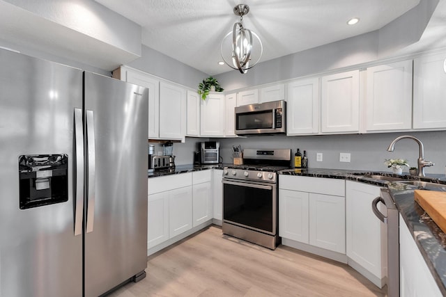 kitchen with a sink, white cabinets, appliances with stainless steel finishes, light wood-type flooring, and dark stone countertops