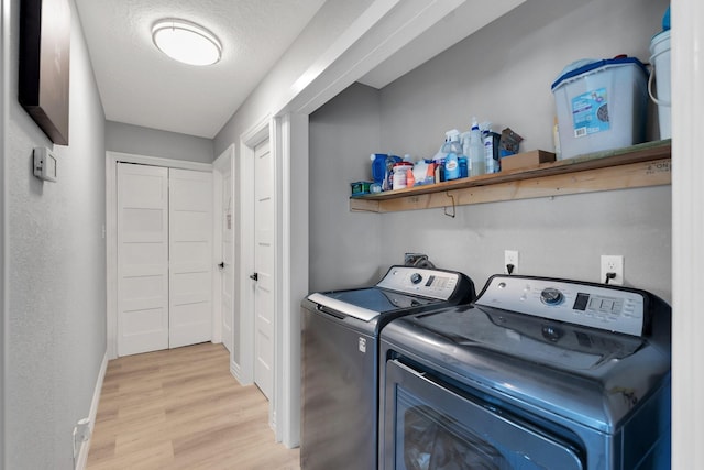 laundry area with washing machine and clothes dryer, light wood-style flooring, a textured ceiling, laundry area, and baseboards