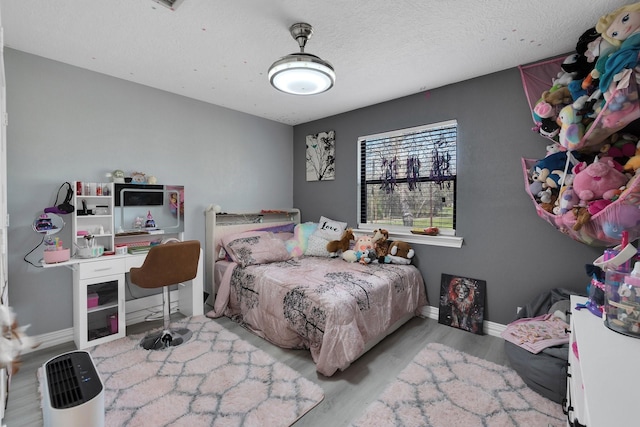 bedroom featuring a textured ceiling, baseboards, and wood finished floors