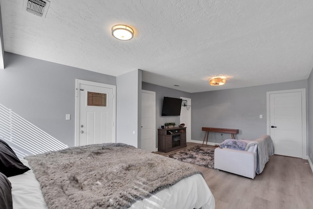 bedroom featuring light wood-style floors, visible vents, and a textured ceiling