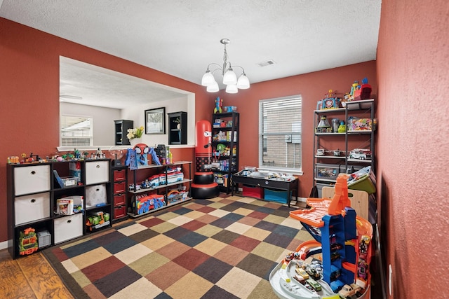 game room with a healthy amount of sunlight, a notable chandelier, and a textured ceiling