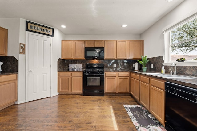 kitchen with dark countertops, black appliances, dark wood-style flooring, and a sink