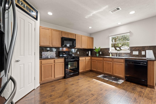 kitchen featuring a sink, visible vents, decorative backsplash, black appliances, and dark wood finished floors