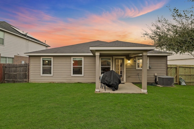 back of property at dusk with fence, a lawn, and central AC unit