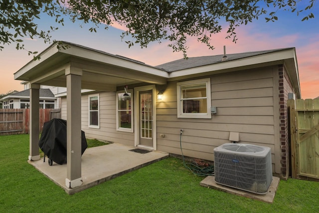 back of property at dusk featuring central air condition unit, a patio area, fence, and a lawn