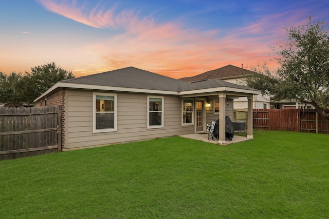 back of house at dusk featuring a fenced backyard, roof with shingles, cooling unit, a yard, and a patio area