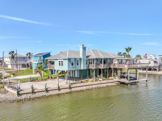 back of house featuring a water view, concrete driveway, a residential view, a carport, and a chimney