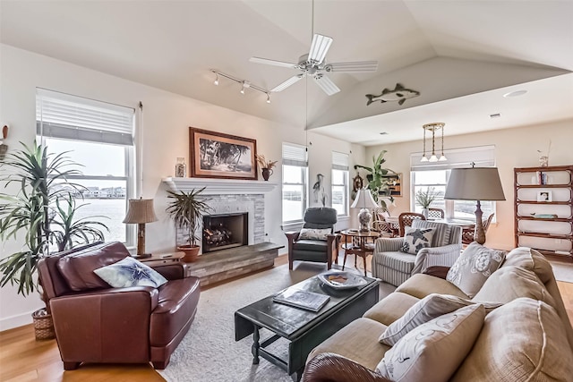 living room with a ceiling fan, lofted ceiling, a fireplace, and light wood finished floors