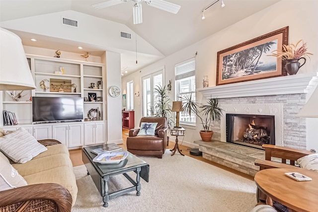 living room featuring light wood-style flooring, a fireplace, visible vents, a ceiling fan, and vaulted ceiling