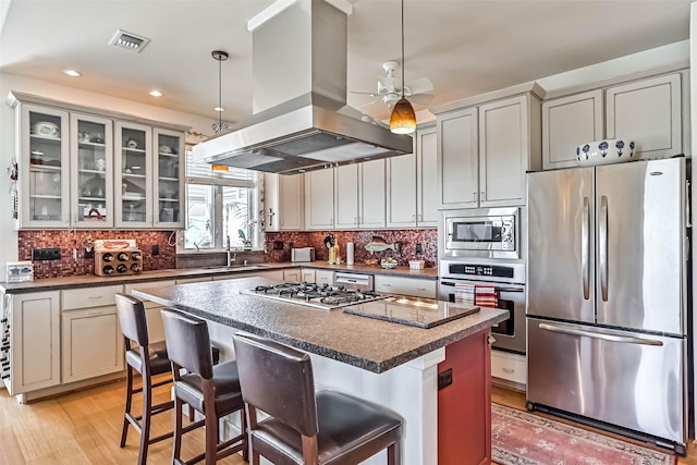 kitchen with appliances with stainless steel finishes, dark countertops, island exhaust hood, and tasteful backsplash