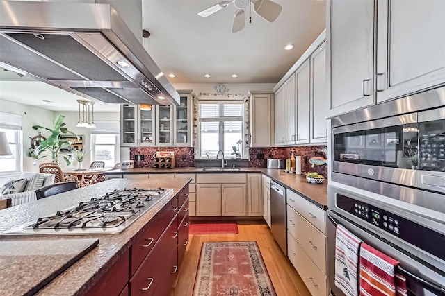 kitchen with appliances with stainless steel finishes, a sink, extractor fan, light wood-style floors, and backsplash