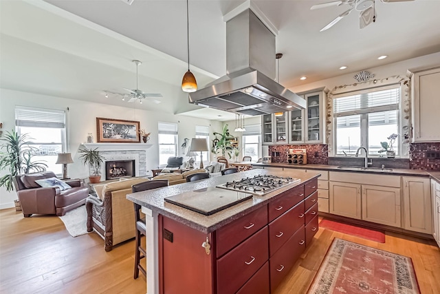 kitchen with a sink, a kitchen island, light wood-style floors, island exhaust hood, and stainless steel gas stovetop