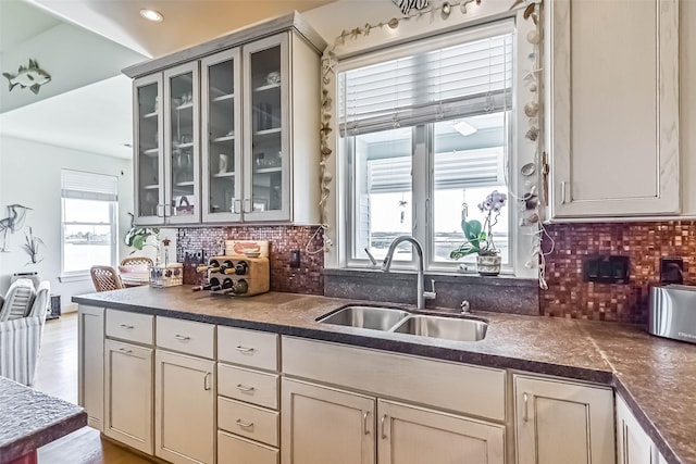 kitchen with glass insert cabinets, dark countertops, a sink, and decorative backsplash