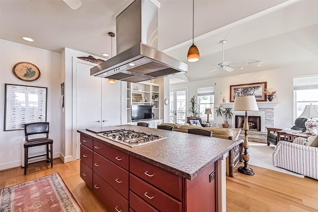 kitchen featuring light wood finished floors, plenty of natural light, island exhaust hood, a fireplace, and stainless steel gas cooktop