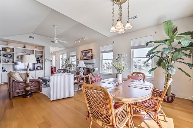 dining room with vaulted ceiling, light wood-type flooring, a fireplace, and visible vents