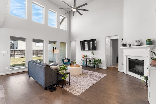 living room featuring a ceiling fan, a glass covered fireplace, dark wood-style flooring, and baseboards