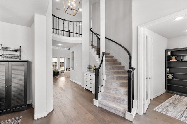 foyer entrance with baseboards, wood finished floors, an inviting chandelier, a high ceiling, and stairs