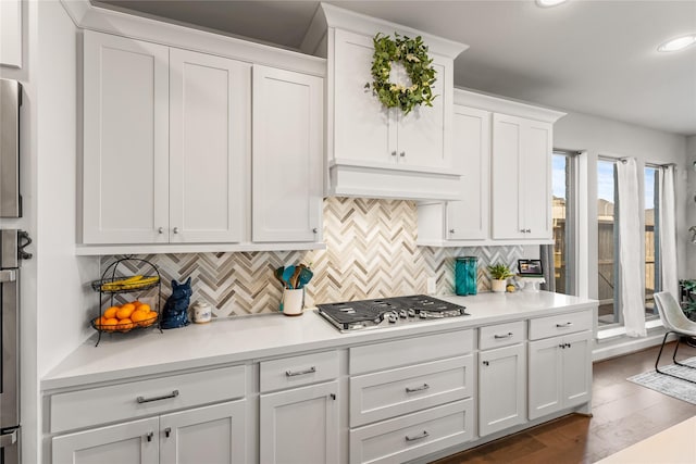 kitchen with custom range hood, stainless steel gas stovetop, white cabinetry, and light countertops