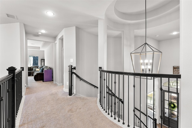 hall featuring an inviting chandelier, visible vents, carpet flooring, and an upstairs landing