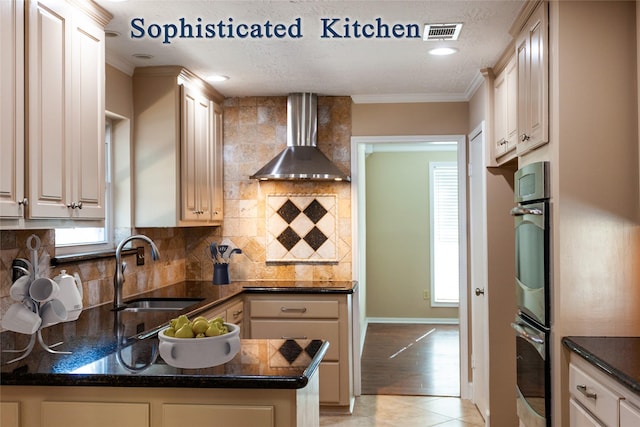 kitchen with visible vents, dark countertops, wall chimney exhaust hood, crown molding, and a sink