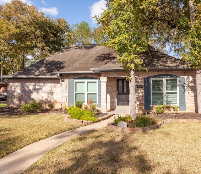 ranch-style house featuring a shingled roof, brick siding, and a front lawn