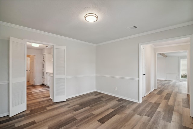 spare room with baseboards, visible vents, wood finished floors, crown molding, and a textured ceiling