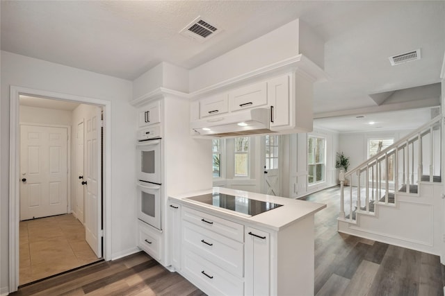 kitchen with a peninsula, white double oven, visible vents, and under cabinet range hood