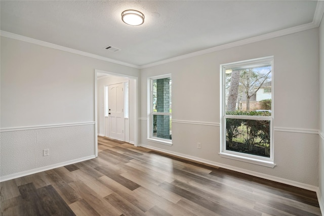 empty room with crown molding, wood finished floors, visible vents, and a healthy amount of sunlight